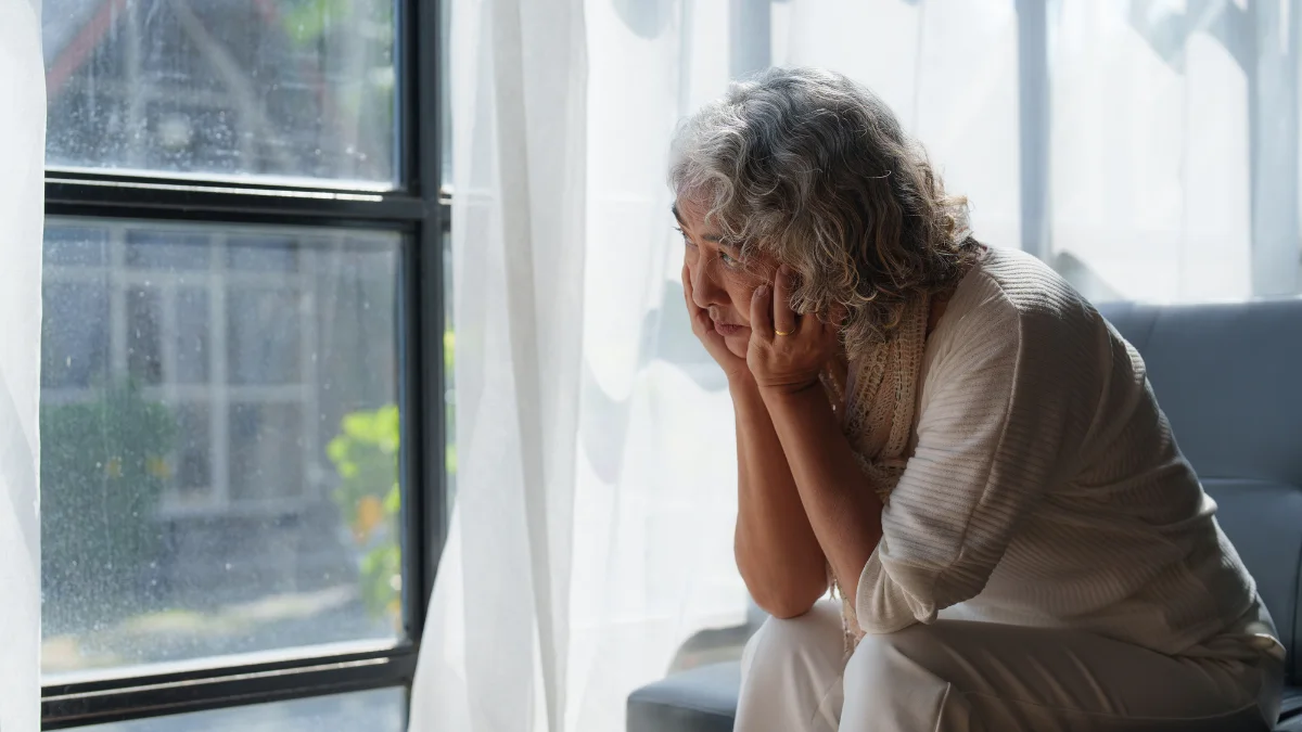 Weary mature woman resting her head in her hands by a window, seeking answers for fatigue in women over 55.