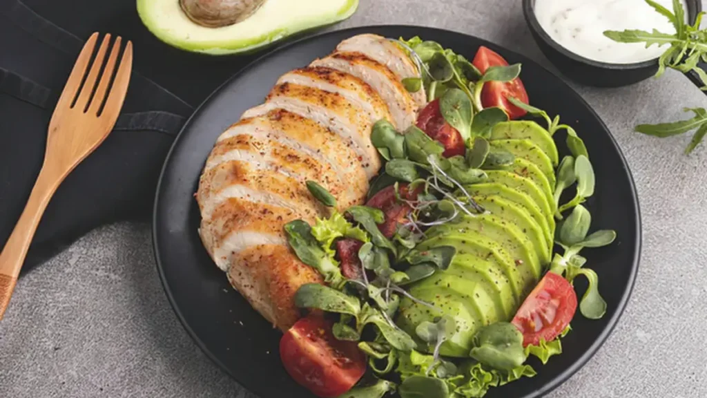 Sliced grilled chicken breast paired with creamy sliced avocado on a dark plate to support muscle protein synthesis.