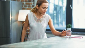 Mature woman reaching for a glass on a kitchen counter to monitor reaction time brain health after 50.