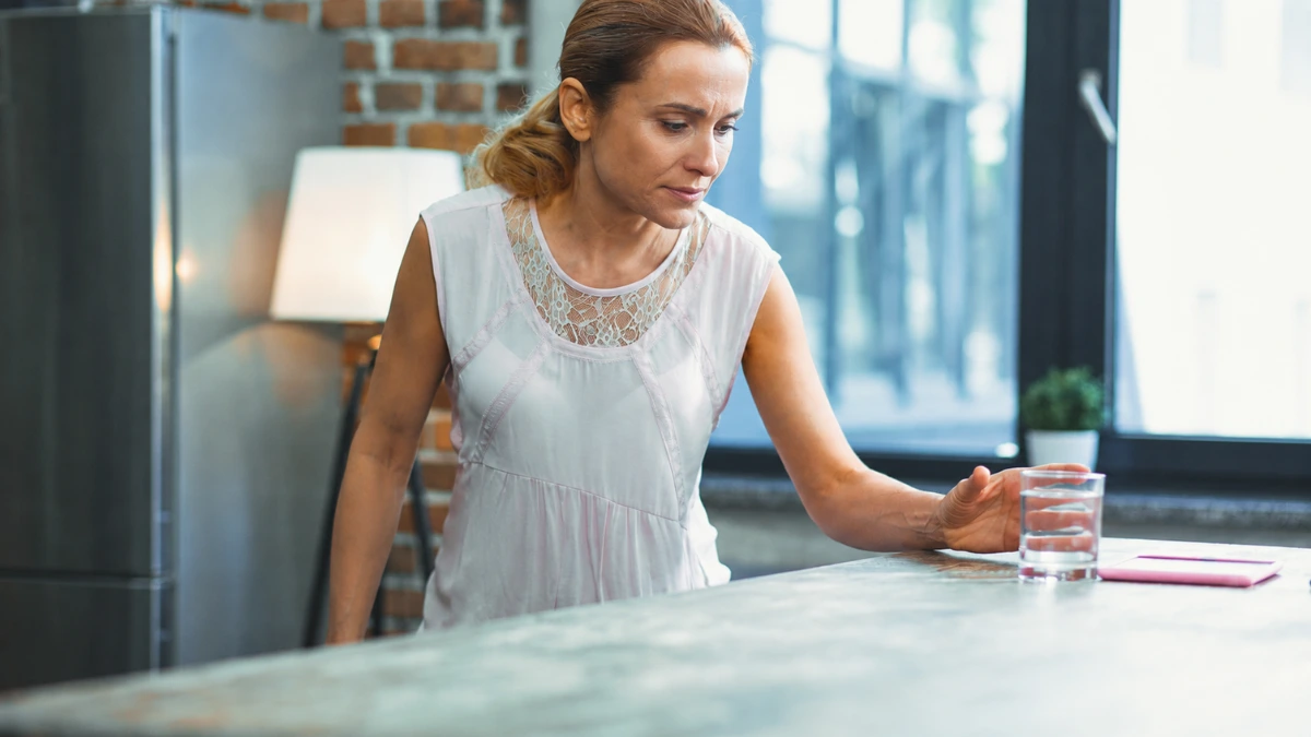 Mature woman reaching for a glass on a kitchen counter to monitor reaction time brain health after 50.
