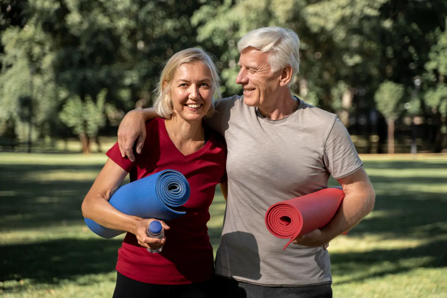 Smiling older couple carrying yoga mats in a sunny park