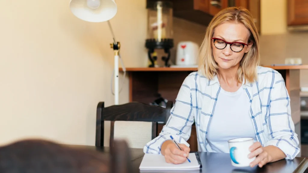 Woman writing a checklist of questions at her kitchen table to prepare for a doctor's appointment