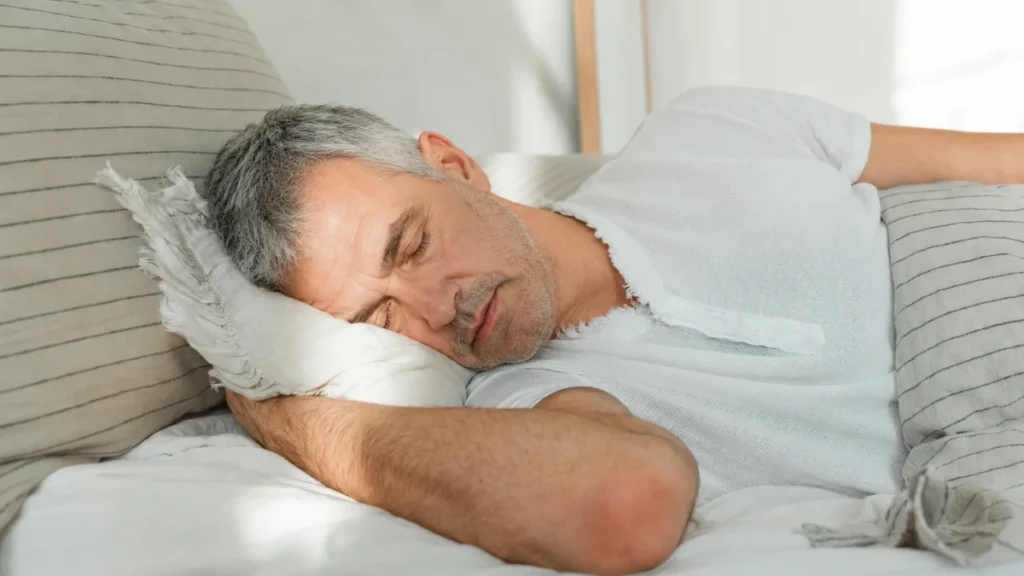 Man sleeping on his side in bed, illustrating how sleep position can factor into next-morning stiffness.
