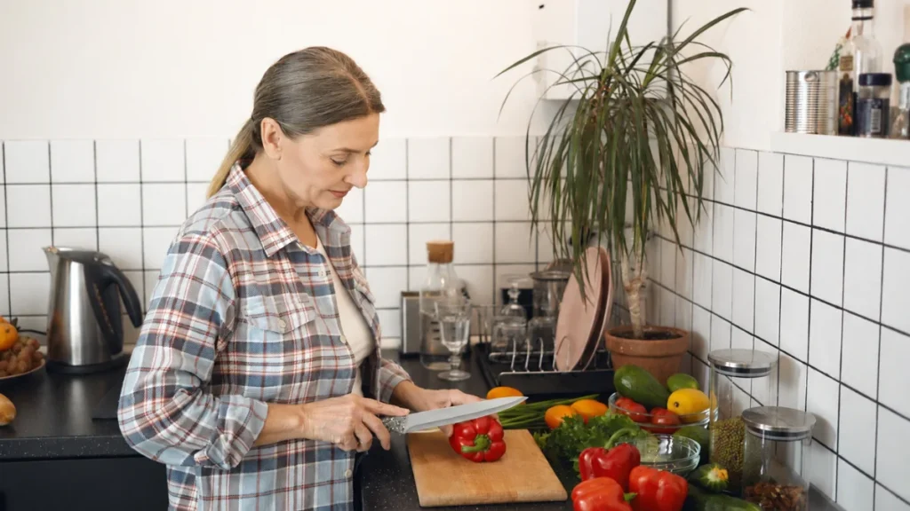 Woman in her 60s slicing fresh vegetables at a kitchen counter, feeding the antioxidant defenses her body already builds.