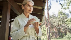 Woman in her 60s pausing on a sunlit porch, carrying the quiet sense of purpose after 50 research ties to a longer life.