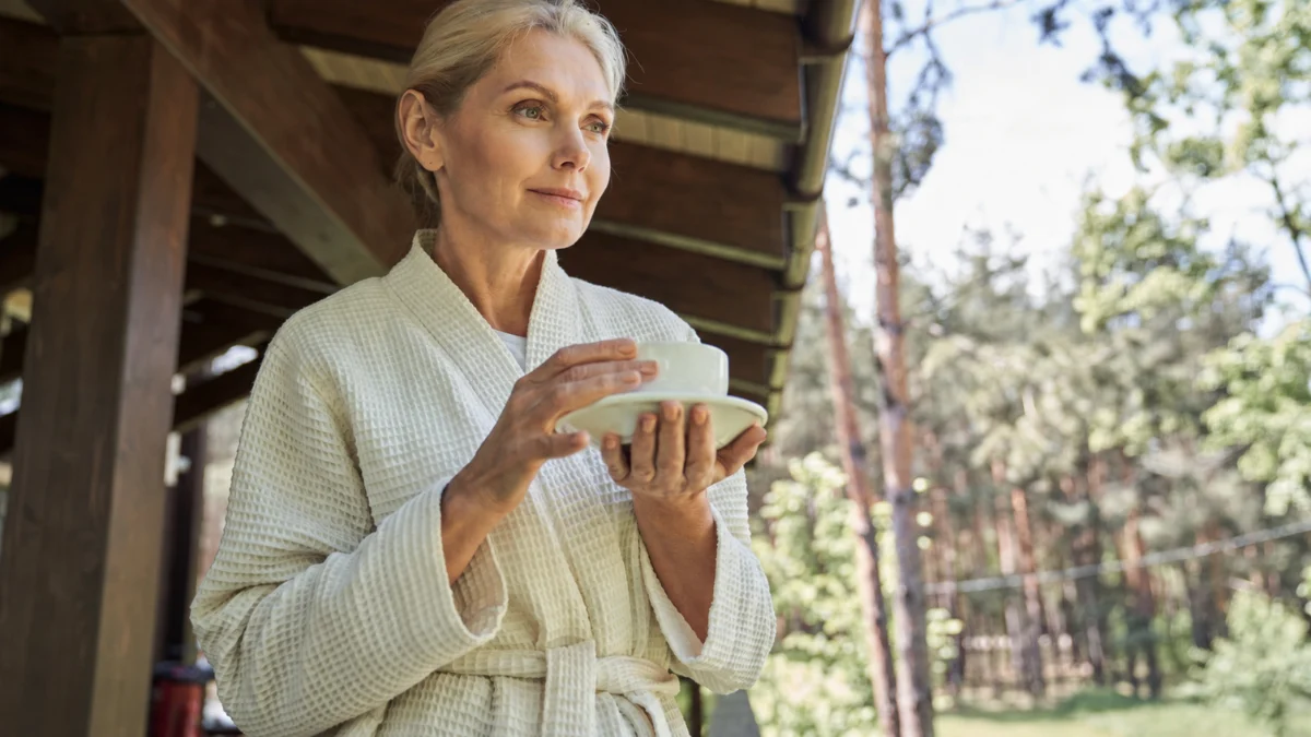 Woman in her 60s pausing on a sunlit porch, carrying the quiet sense of purpose after 50 research ties to a longer life.