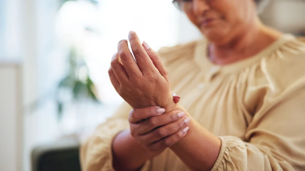 Woman in her sixties cradling a painful wrist at home, experiencing the joint discomfort the article links to high-heat cooking habits.
