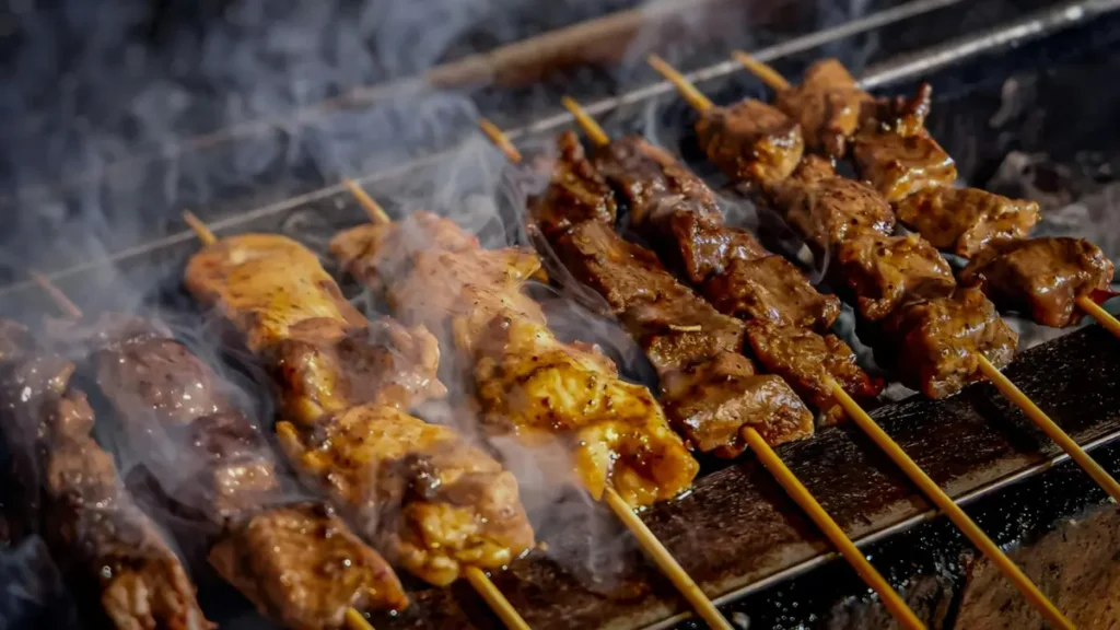 Meat skewers charring on a grill grate with smoke rising, showing the high-heat browning that signals harmful compound formation during grilling.