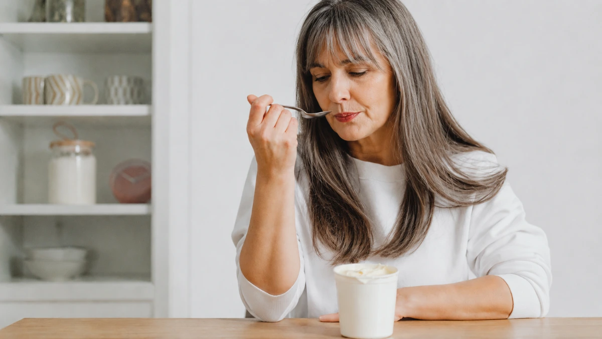 Woman in her 60s at kitchen table carefully eating a small portion of plain yogurt during a cautious gut reintroduction after a dietary pause.