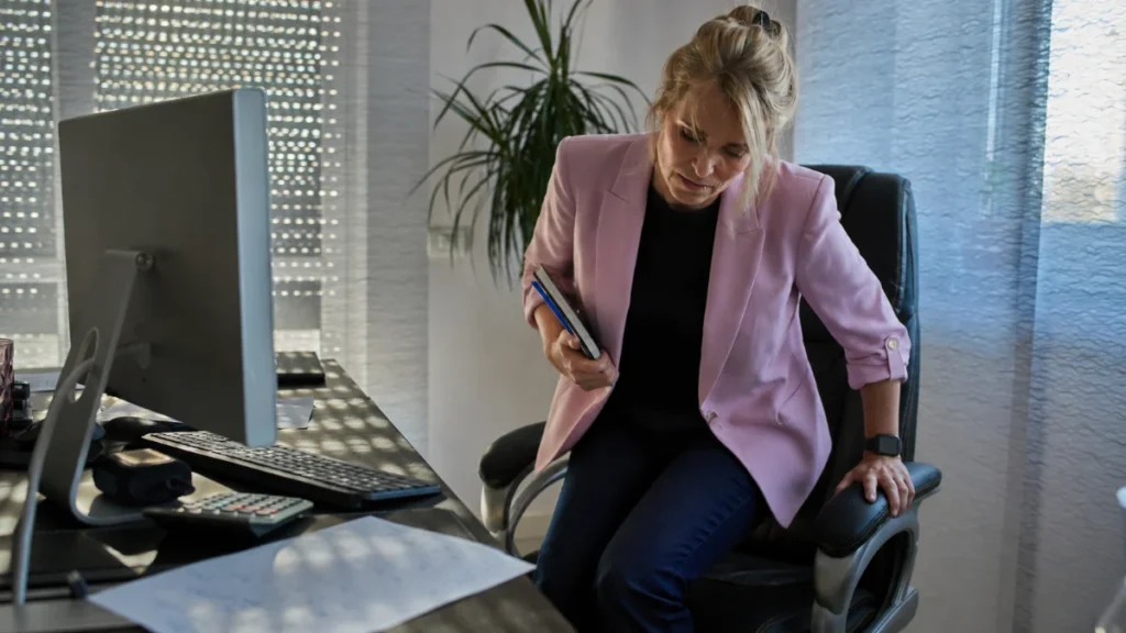Woman in her 50s rising from a home desk chair to take a standing break, relieving prolonged sitting pressure on peripheral nerves.