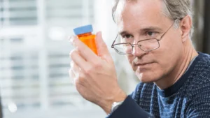 Man in his 50s holding a prescription bottle at home, questioning whether his low testosterone depression has been correctly diagnosed.