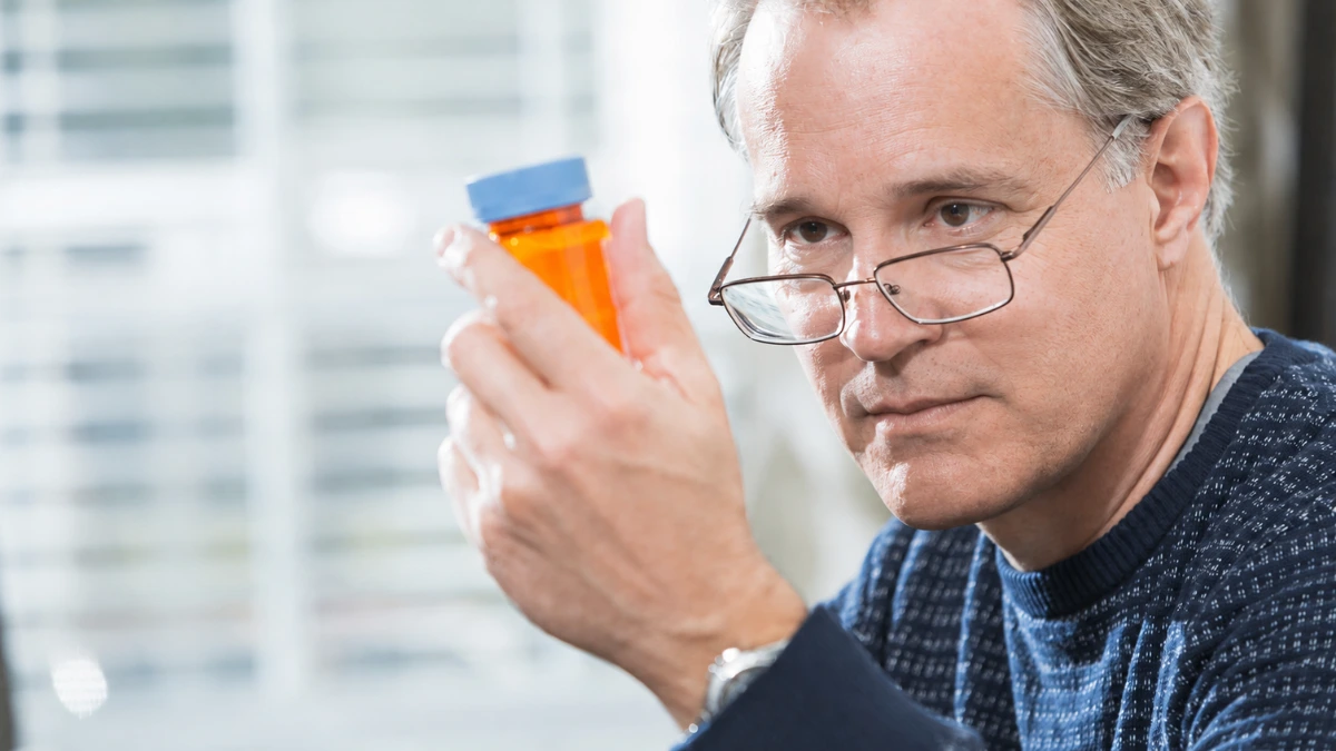 Man in his 50s holding a prescription bottle at home, questioning whether his low testosterone depression has been correctly diagnosed.