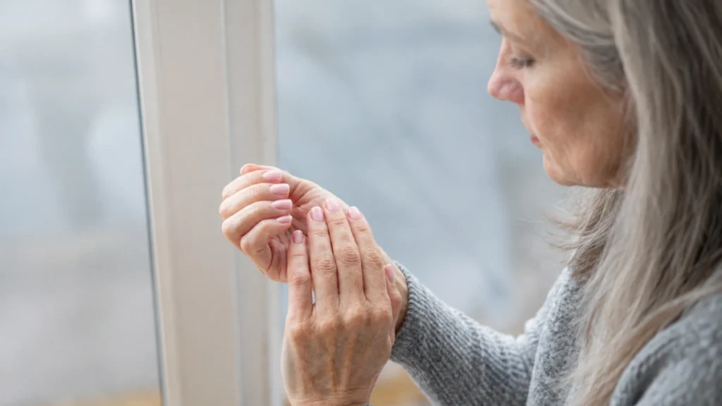 Woman in her 60s examining her fingernails in natural light, checking for unexplained dark lines under the nails.