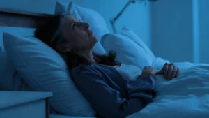 Woman in her 50s awake in a dark bedroom at 3 a.m., unable to sleep — a common sign of magnesium deficiency.