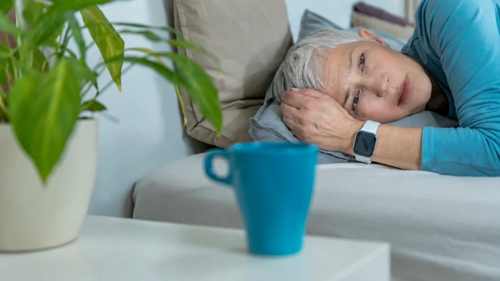 Woman in her 50s lying on a sofa with an unfocused gaze, her expression carrying quiet unexplained unease in a calm room.