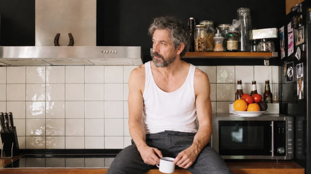 Man in his 60s at kitchen counter with coffee staring blankly as lifestyle inputs quietly alter brain health.